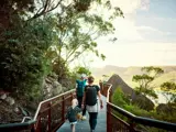 Two parents and a small child walk together on a railed pathway in the Australian bush